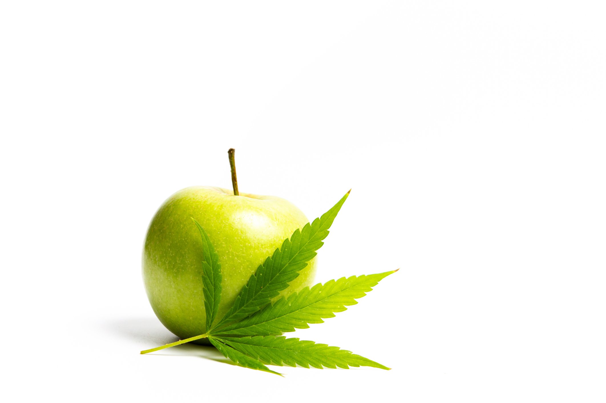 Marijuana leaf in front of a green apple.