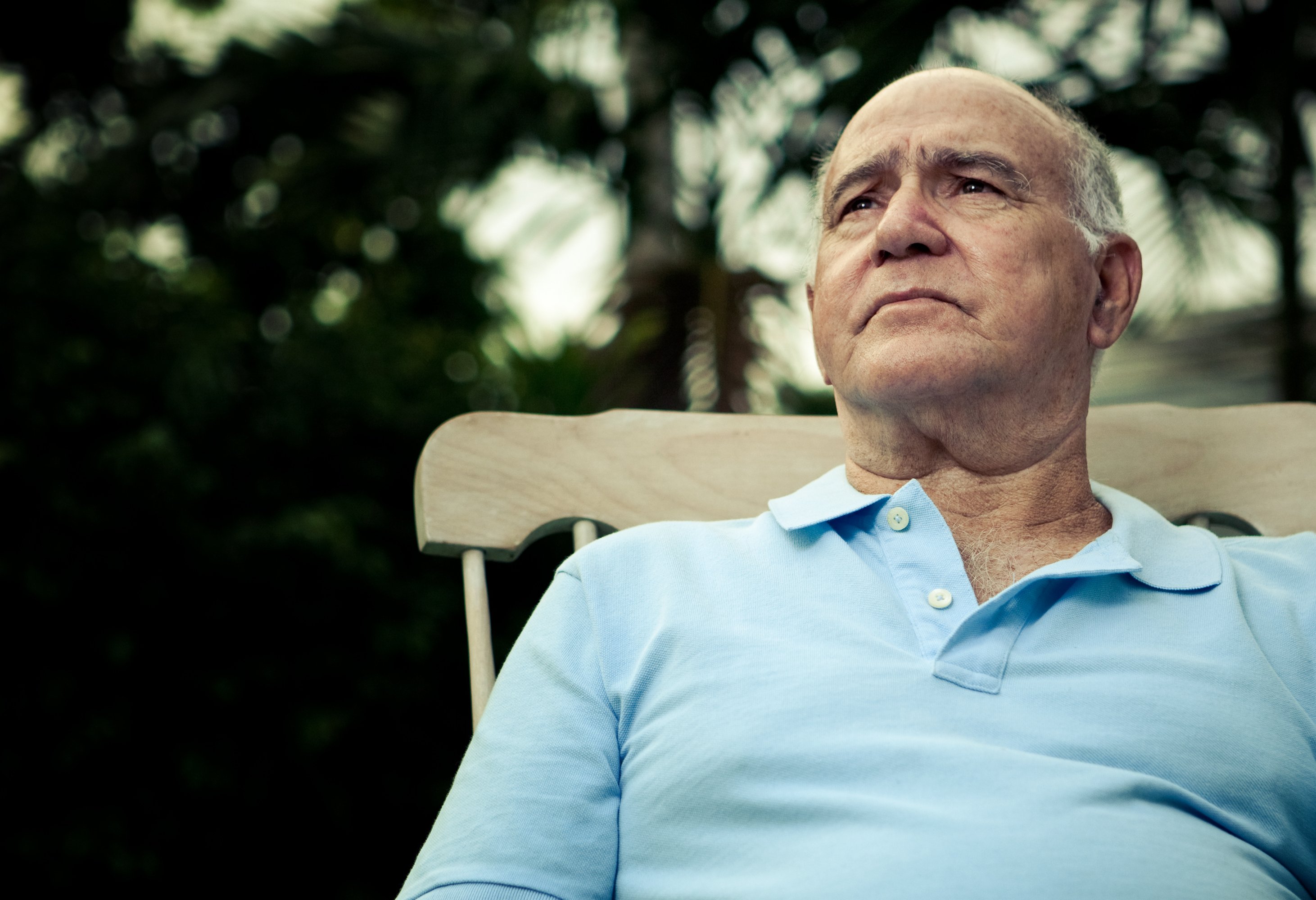 Older man sitting in a rocking chair outside and looking upward.