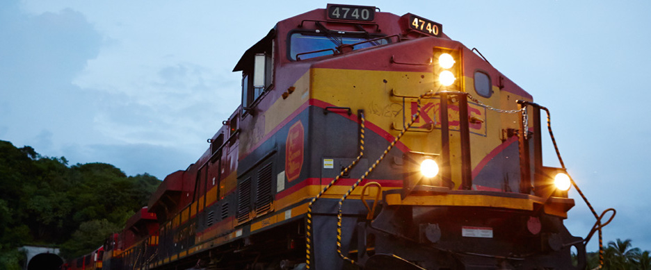 A Kansas City Southern locomotive emerging from a tunnel at dusk.