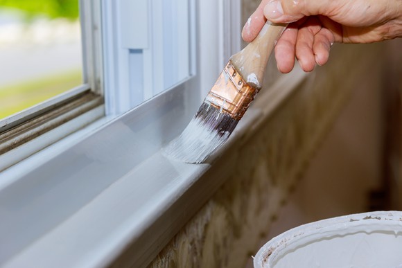 A close-up of a man carefully painting a windowsill. 