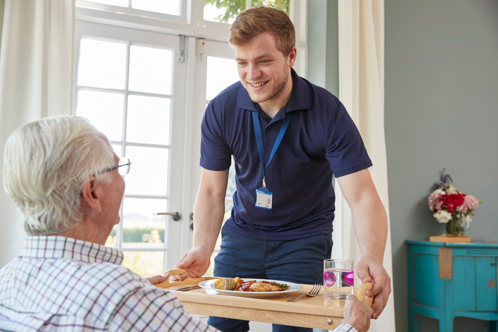 Male service provider bringing a meal to an elderly man.