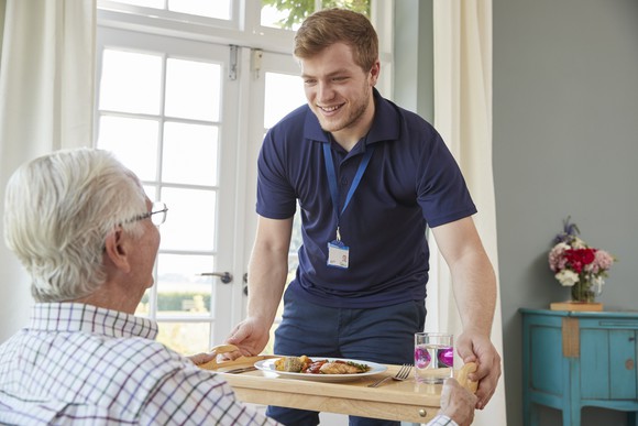 Male service provider bringing a meal to an elderly man.