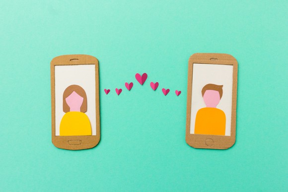 A man and a woman displayed on mobile phones, connected by hearts.