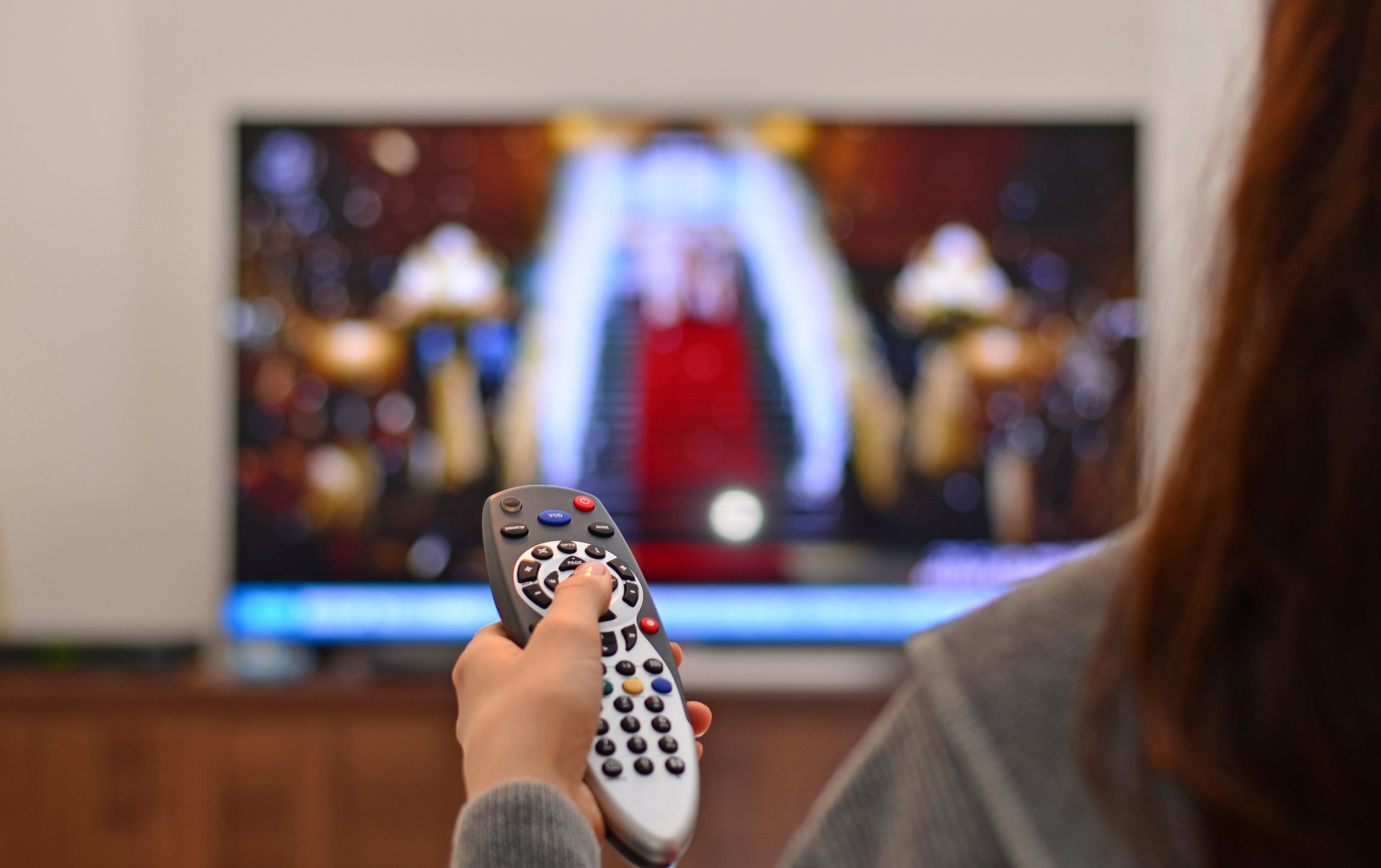 A woman pointing a remote control device at a TV in the background.