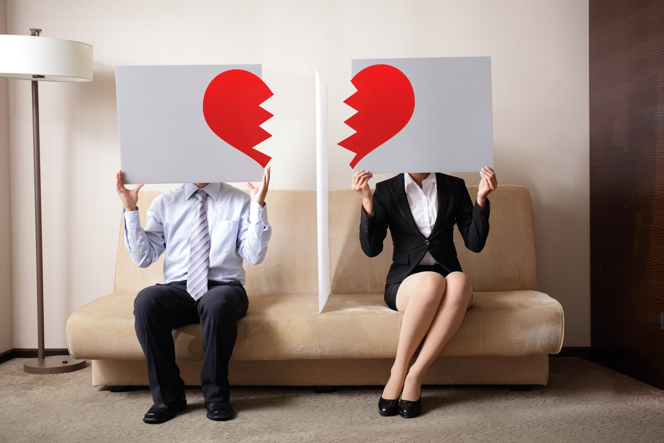 A man and a woman each hold half a torn paper heart.