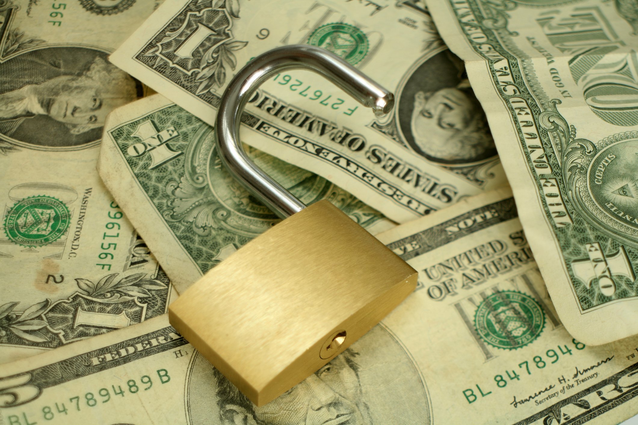 An open padlock sits on top of a scattered pile of U.S. currency.