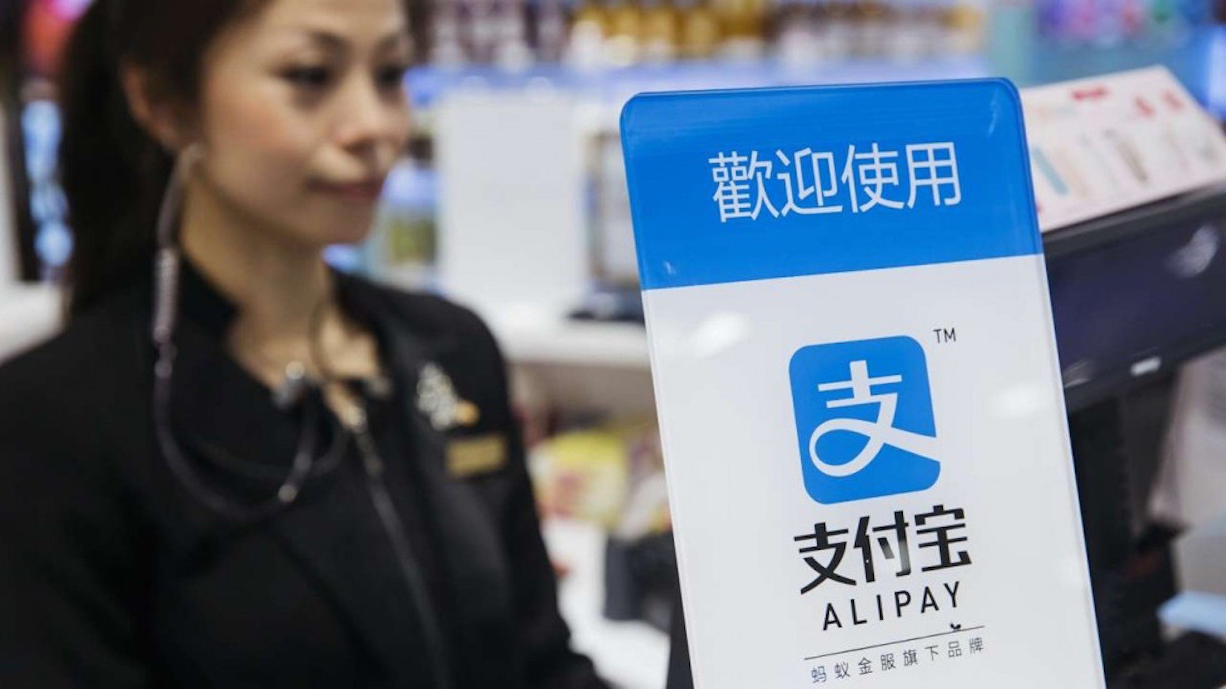 A woman is shown at a grocery checkout that allows customers to use Alipay.