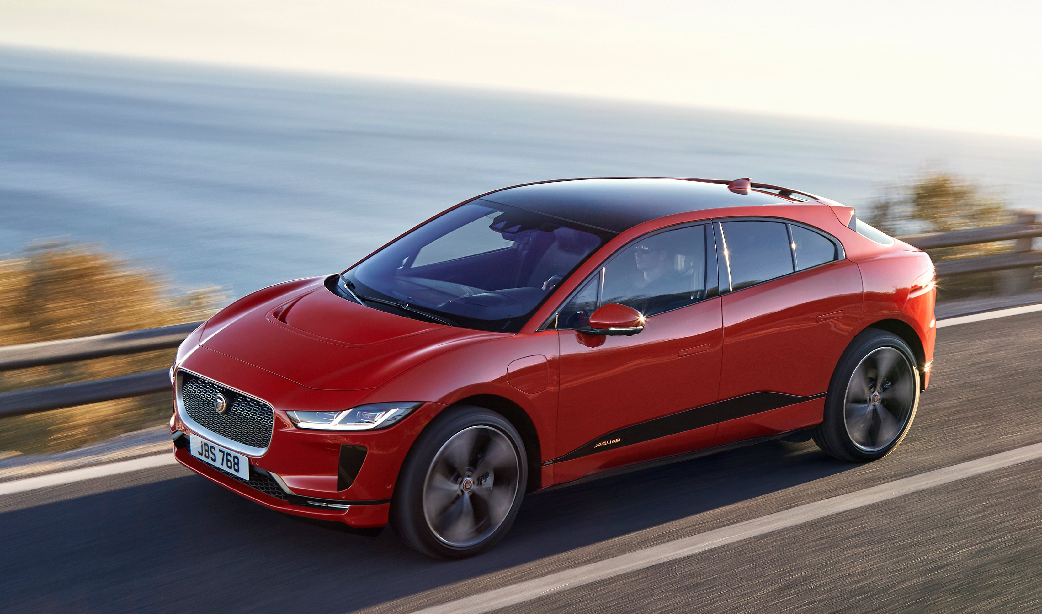 A red Jaguar I-Pace, a sporty electric crossover SUV, on a coastal road