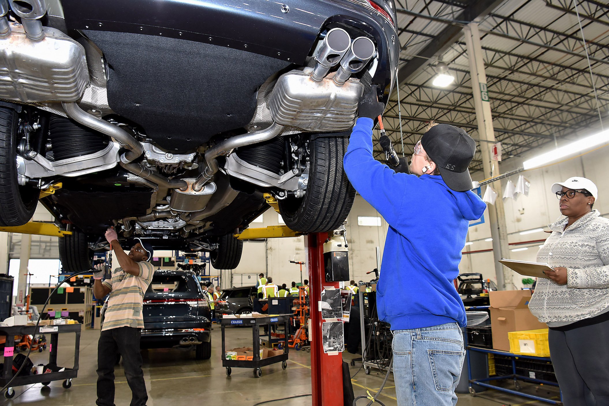 Two workers are shown attaching parts to a 2020 Ford Explorer, a midsize crossover SUV, in a factory setting.