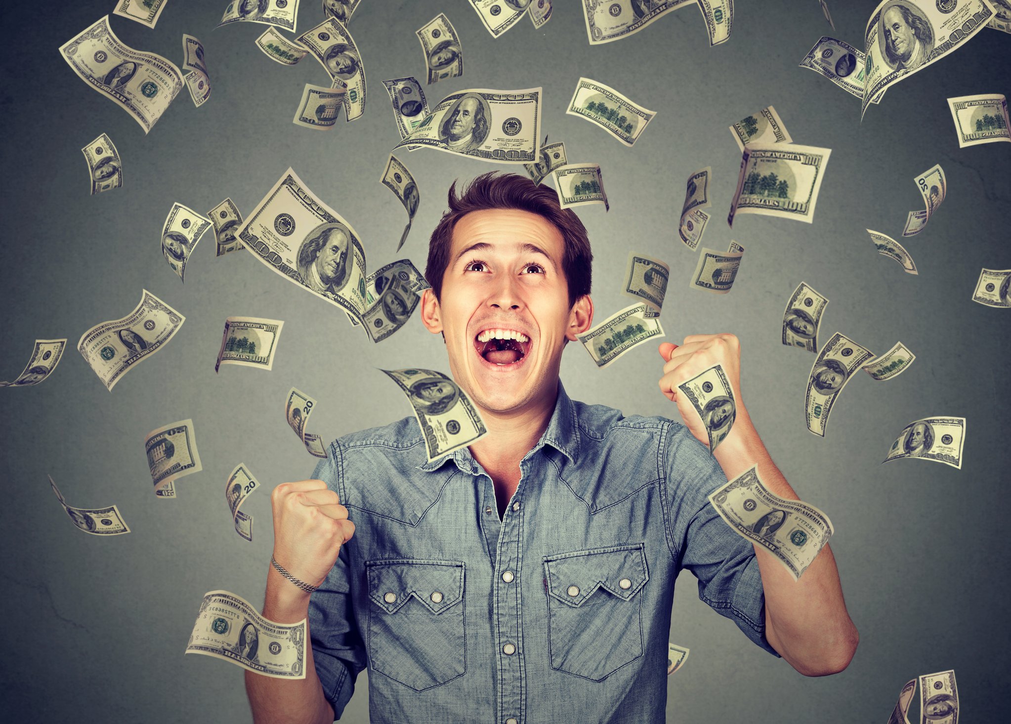 Smiling young man with money falling down on him