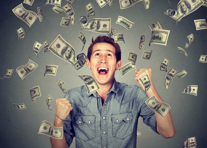 Smiling young man with money falling down on him