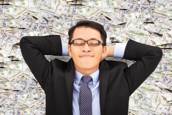 Satisfied guy in a suit resting on a pile of money.