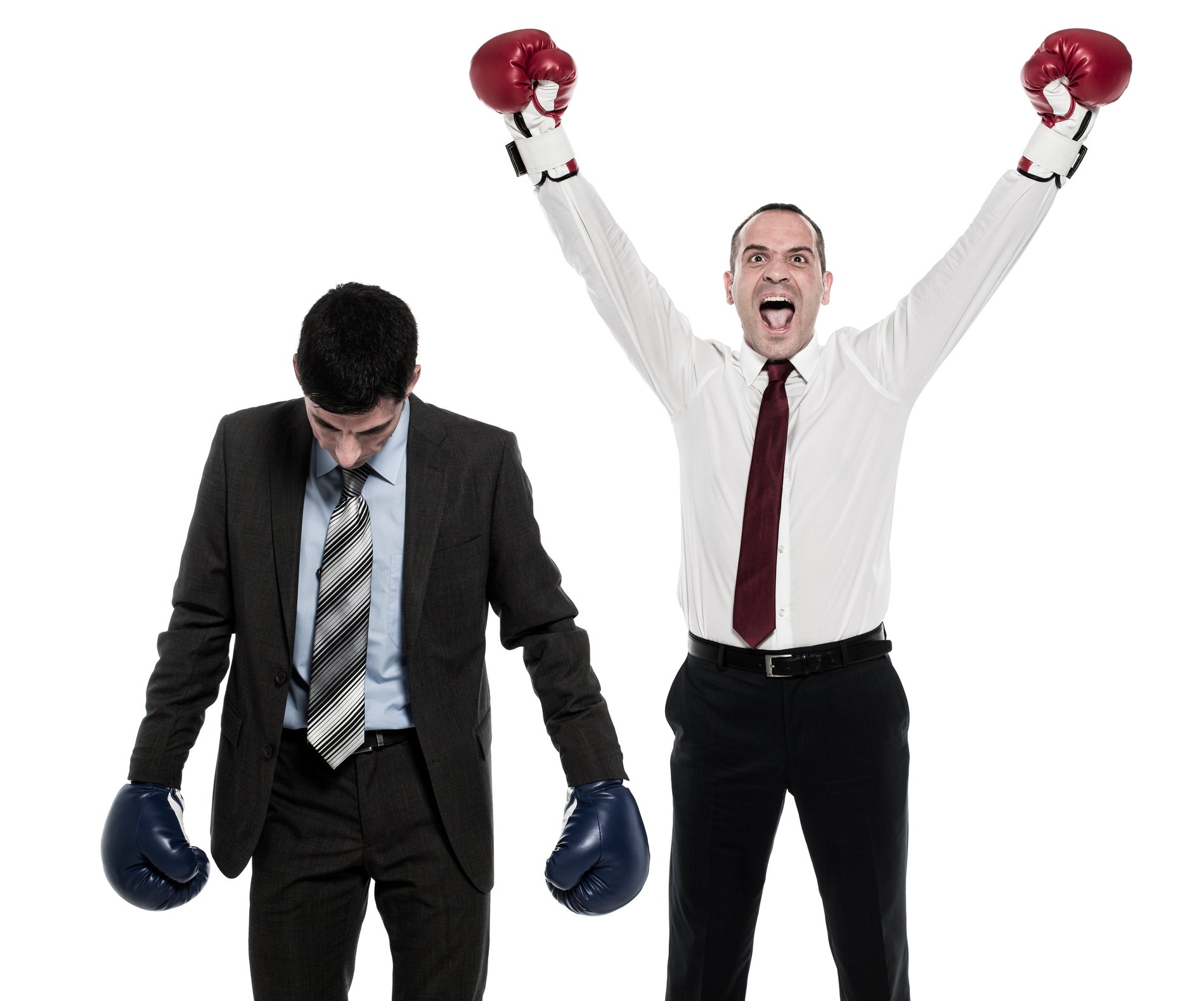 Two men in business attire are wearing boxing gloves. One has his head lowered, while the other has his arms raised in celebration.