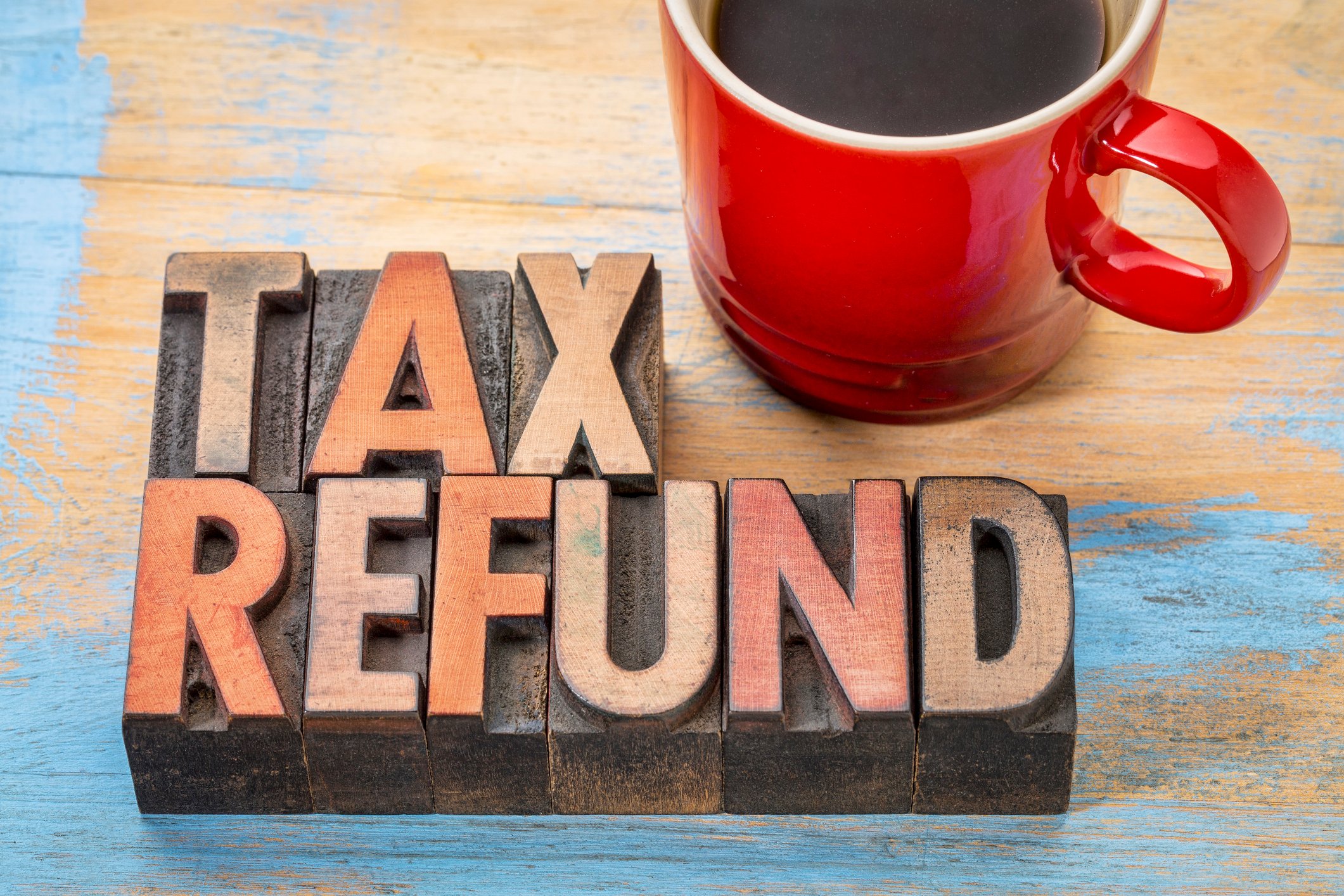 The words "tax refund" spelled out in gold letters on wooden blocks next to a red mug of coffee.