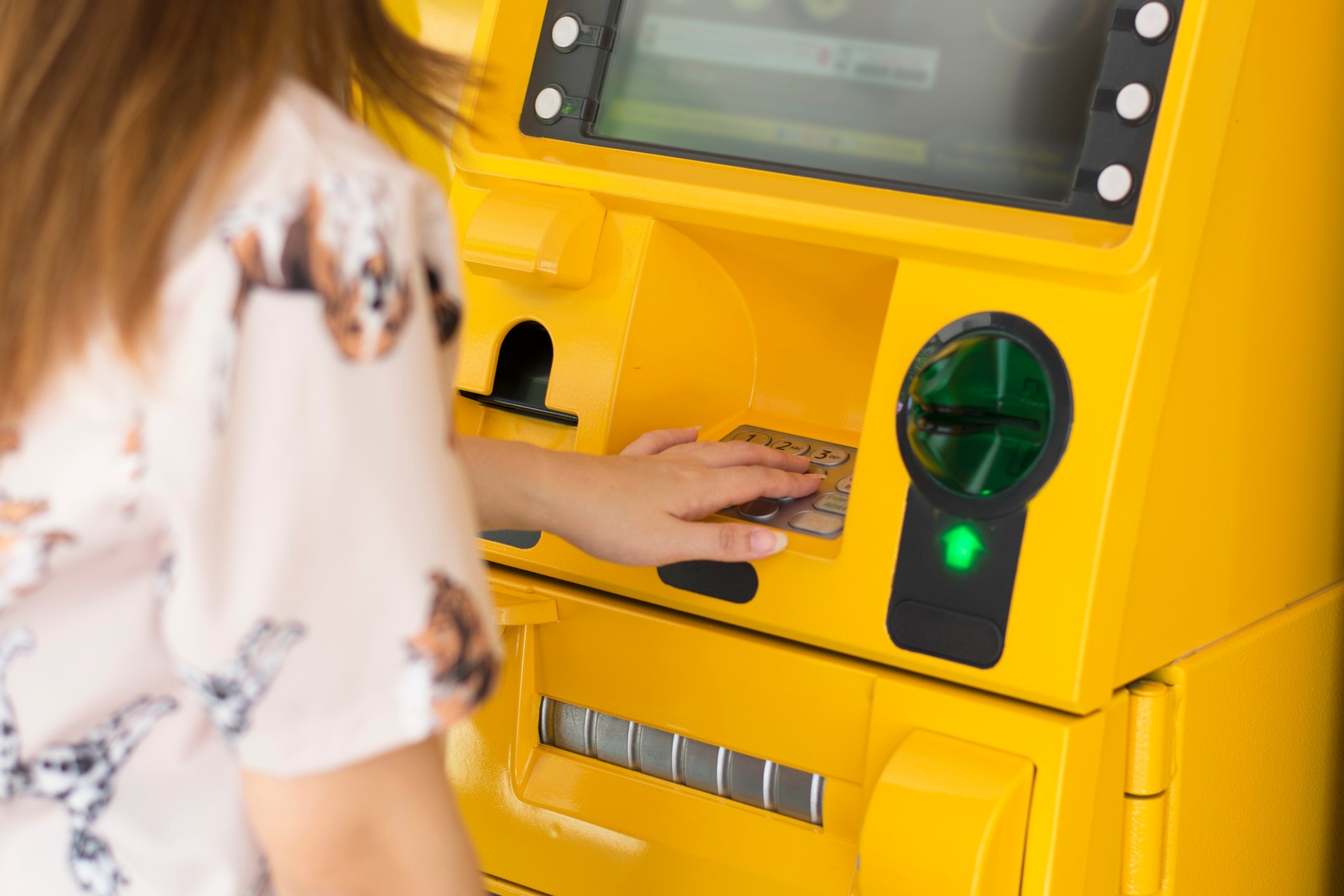 Woman withdrawing funds from a bright yellow ATM machine.