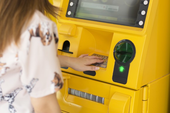 Woman withdrawing funds from a bright yellow ATM machine.