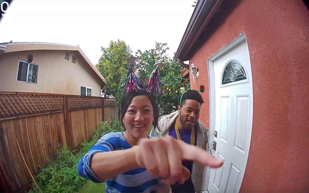 A picture of two people on a doorstep with one about the ring the doorbell.