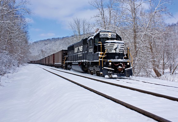 A Norfolk Southern locomotive engine pulls a train through snow.