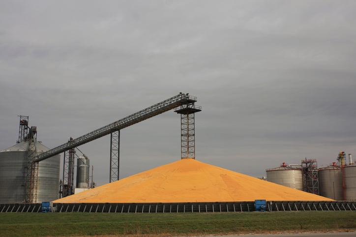 A giant pile of corn kernels next to a grain storage facility.