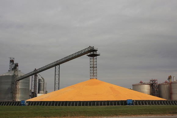 A giant pile of corn kernels next to a grain storage facility.