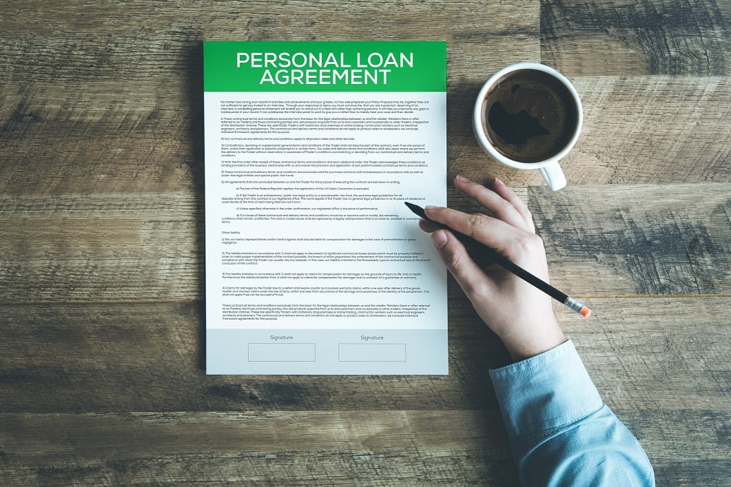 Hand holding a pencil and hovering over a personal loan agreement.