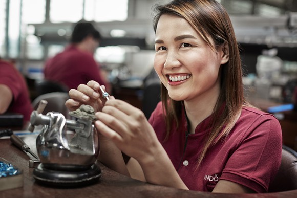 A Pandora worker smiles as she works on assembling a charm.