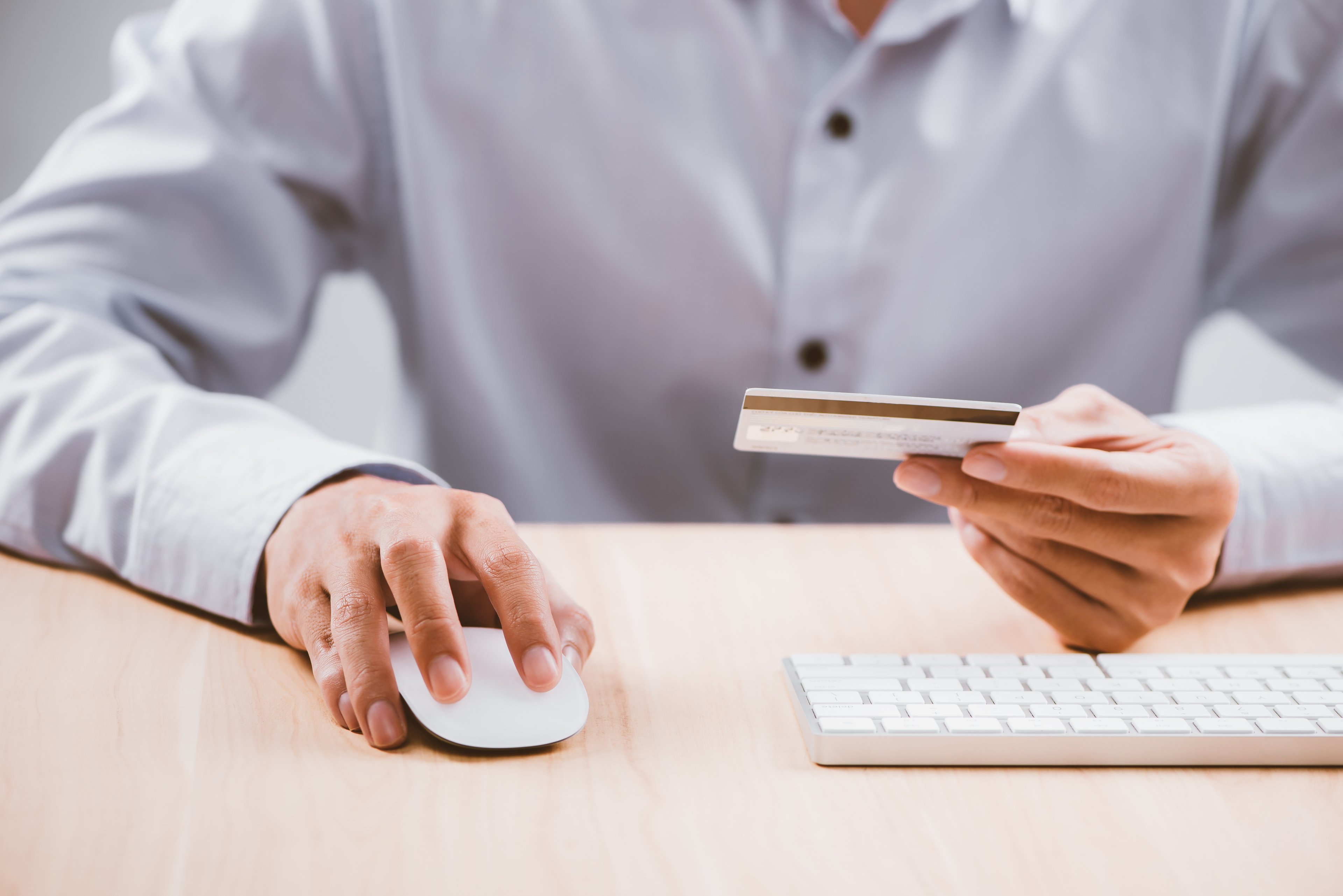 A man holds a computer mouse in one hand and a credit card in the other. 