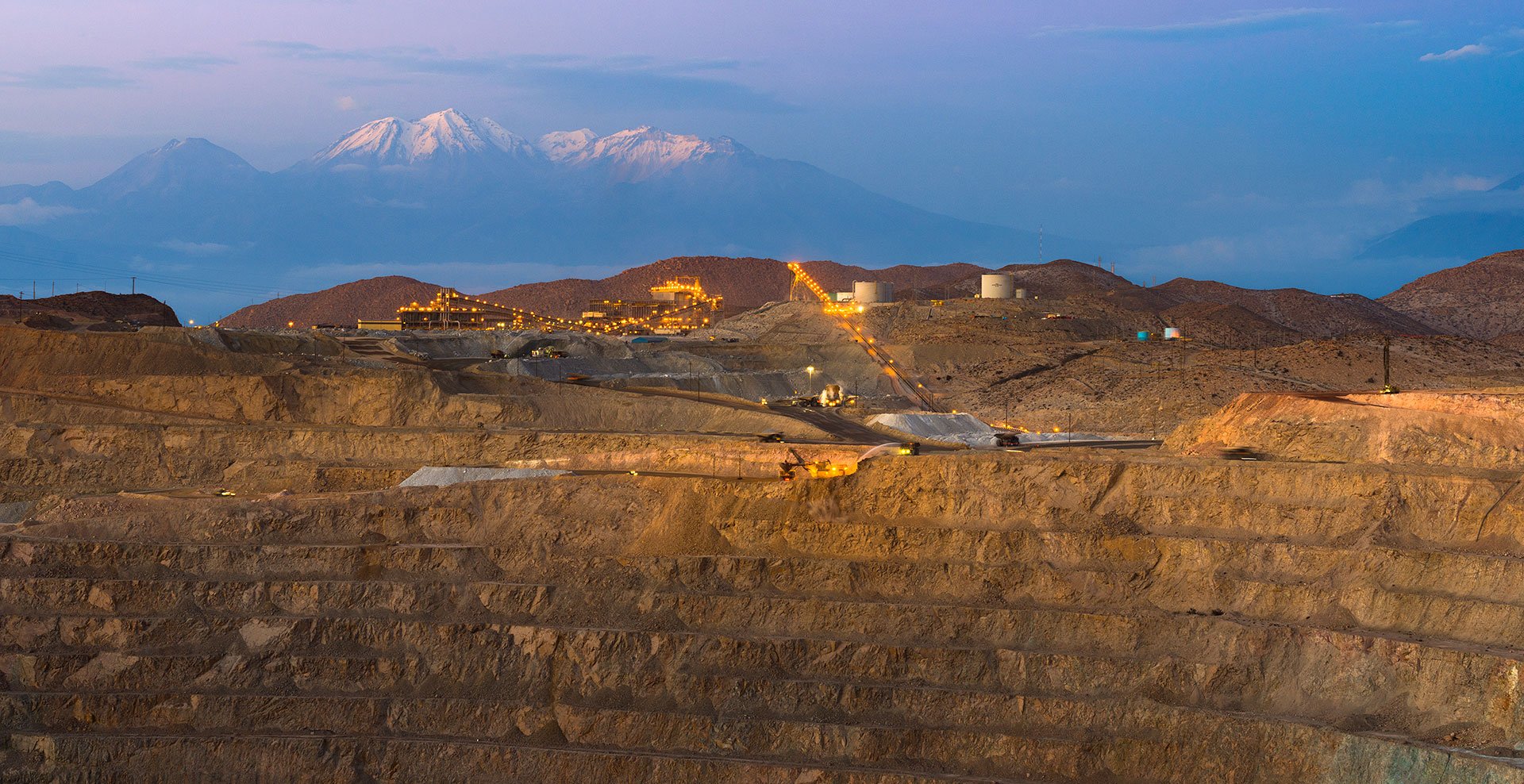 Open-pit mining operation with equipment near the top of the mine, with mountains in the background.