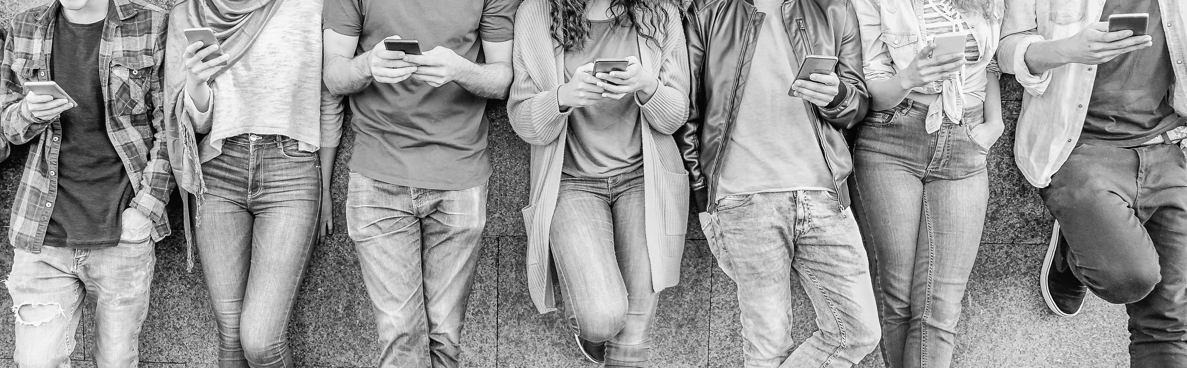 A black and white image of several millennials on their smartphones.