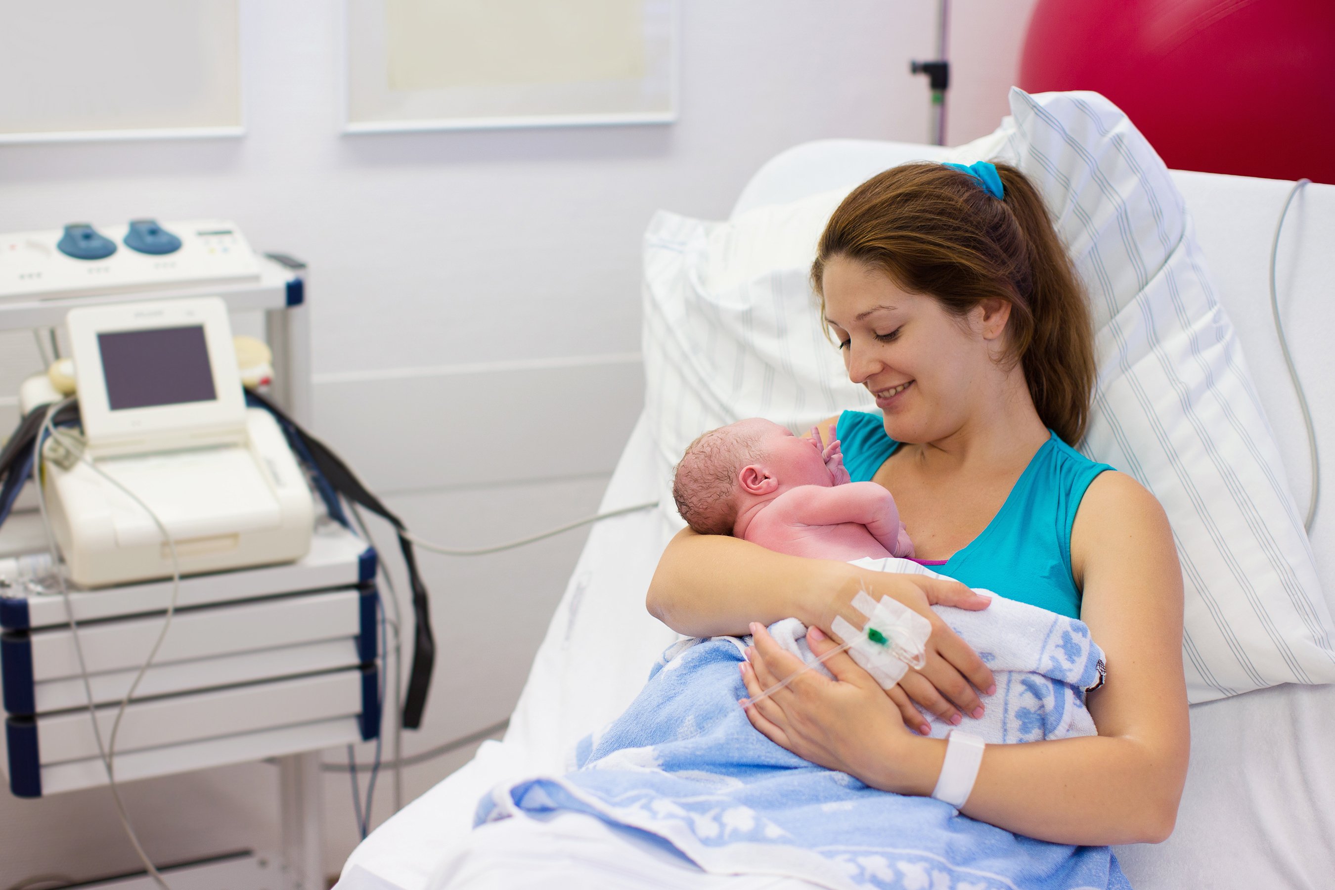 Mom attached to monitoring machine holding a newborn in a hospital bed.