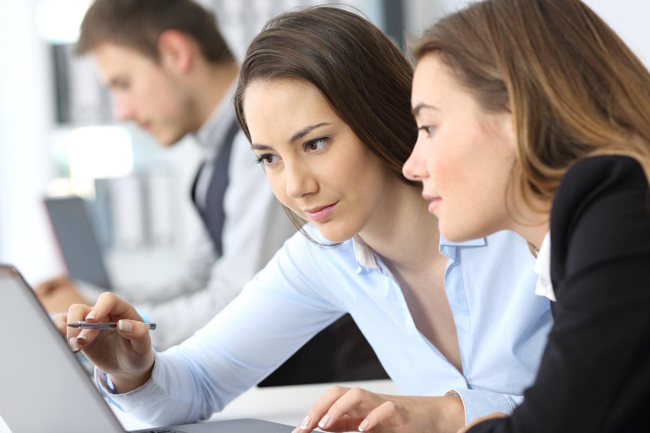 A woman helps another at a computer.