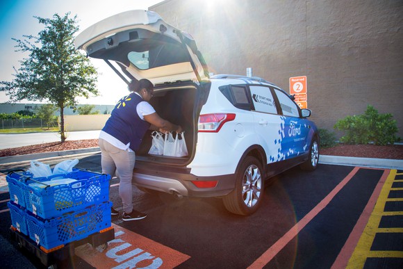 A Walmart employee loading grocery bags into the back of a Ford car.