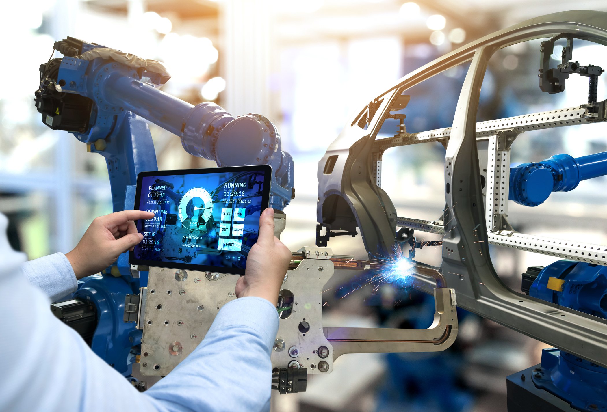 An automotive engineer uses a tablet to monitor an assembly line.
