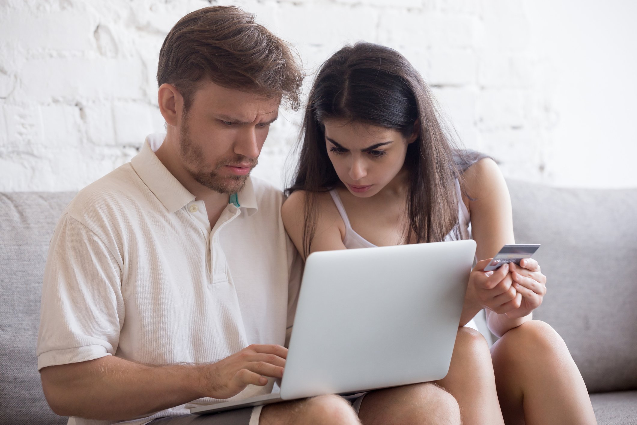 Couple looking at laptop; man has confused expression and woman holds a credit card.