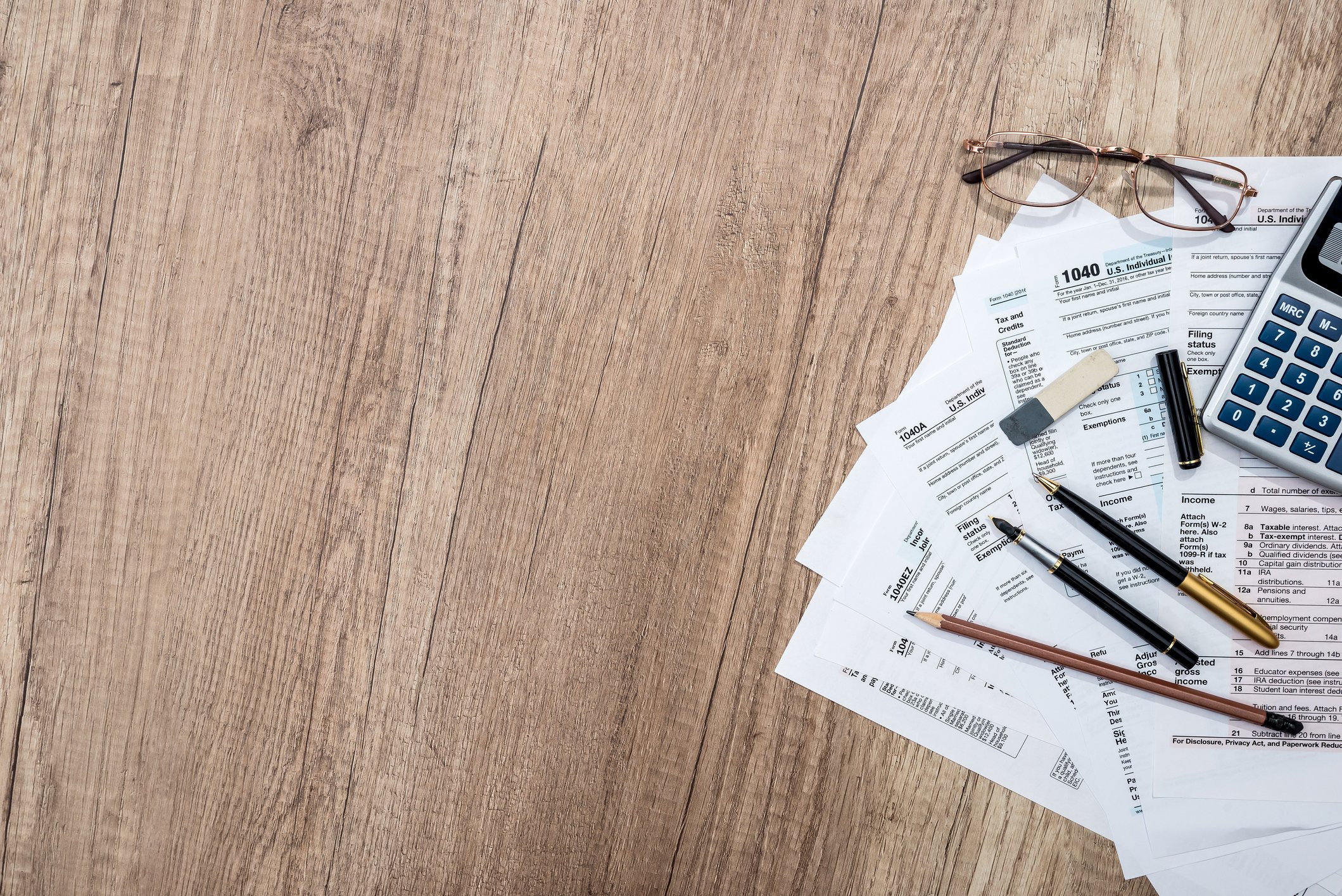Tax forms, pens, glasses, and calculator resting on wooden surface