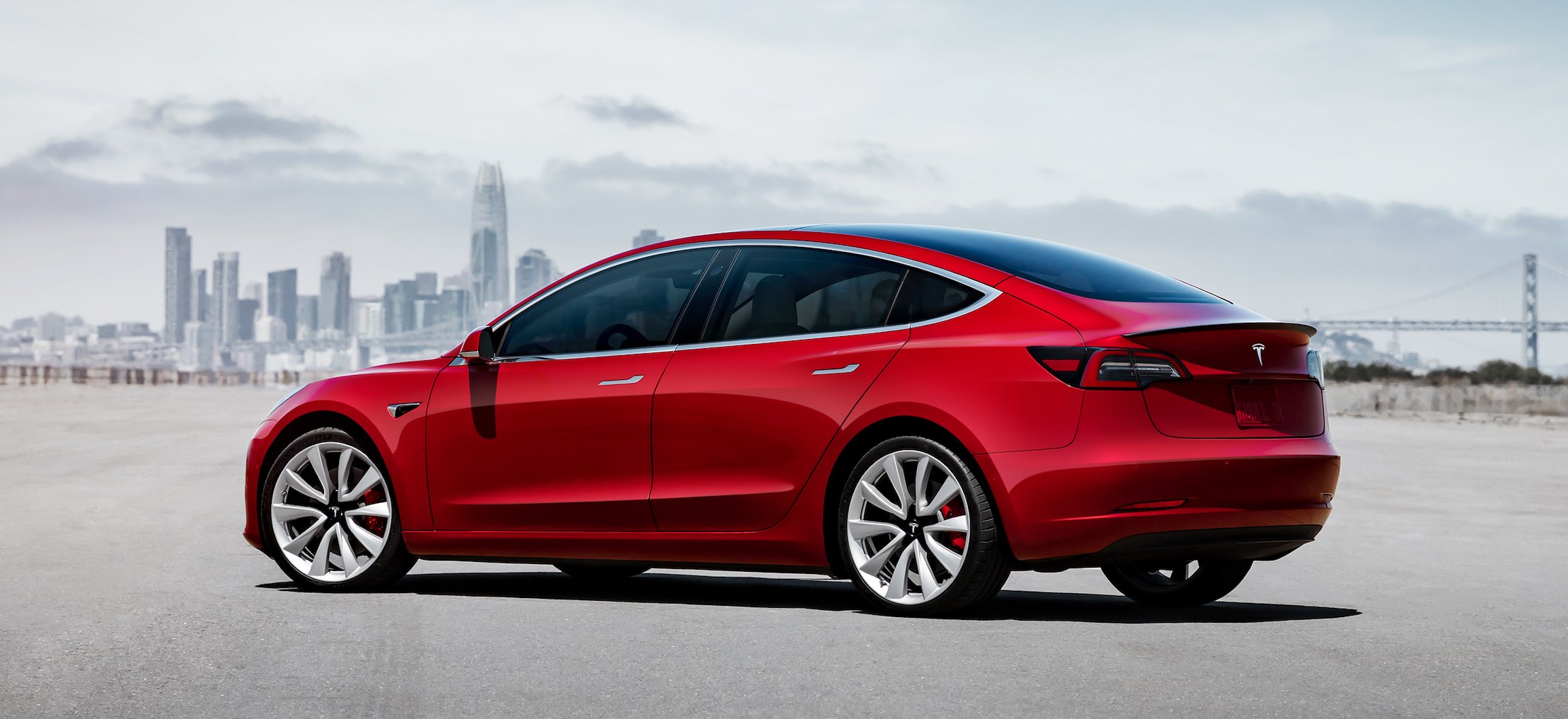 A red Tesla Model 3, a sleek compact luxury-sports sedan