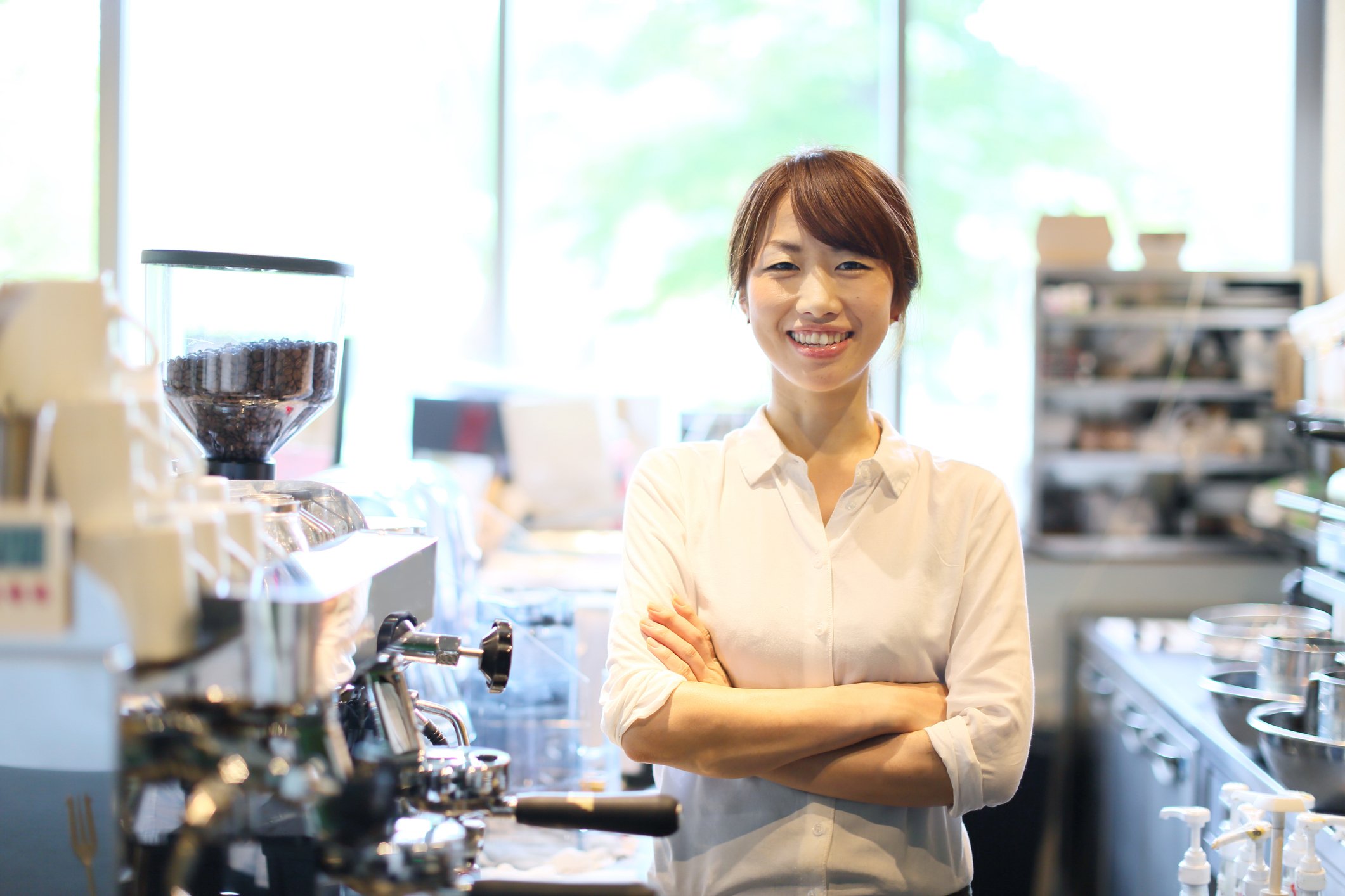 A female entrepreneur stands near the espresso machine in her coffee shop.