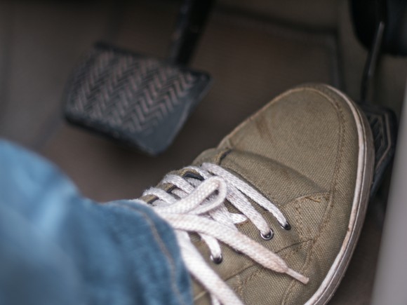 A sneakered foot stepping on a gas pedal