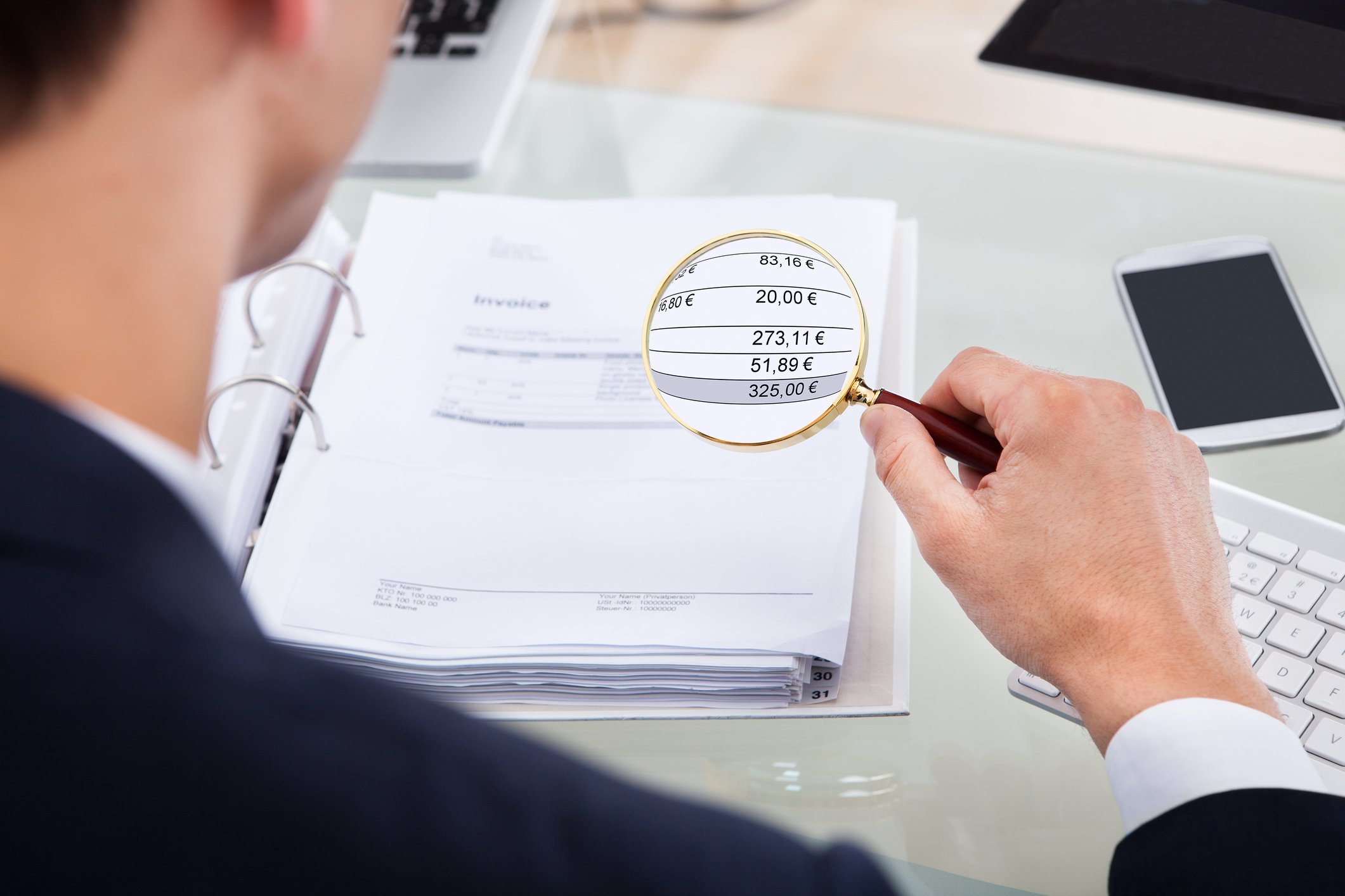 Person holding magnifying glass over financial ledger