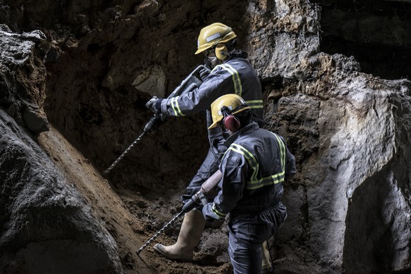 A pair of workers in helmets carrying drills in a subterranean environment