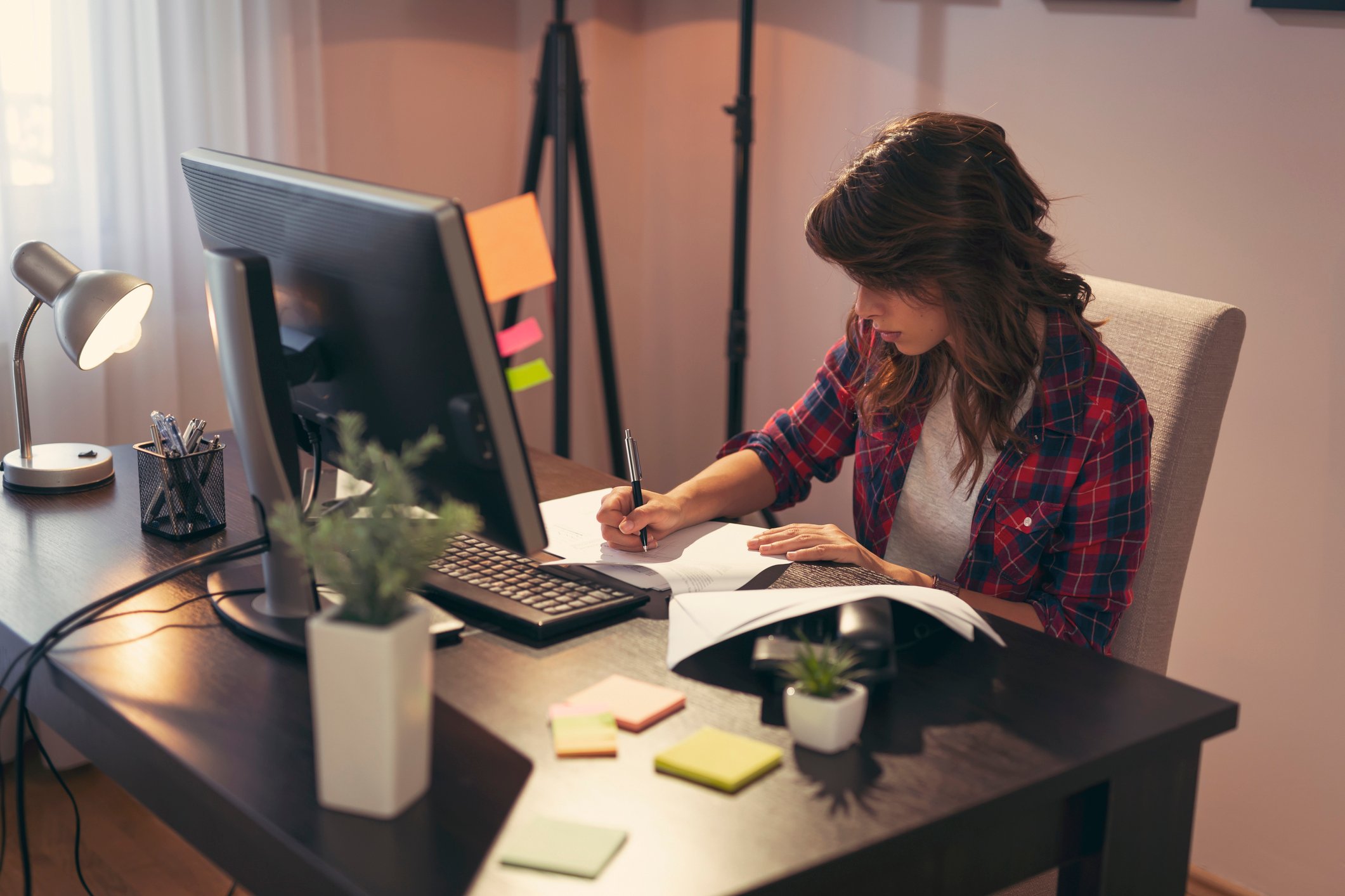 A woman sitting at an office desk takes notes in front of a computer.
