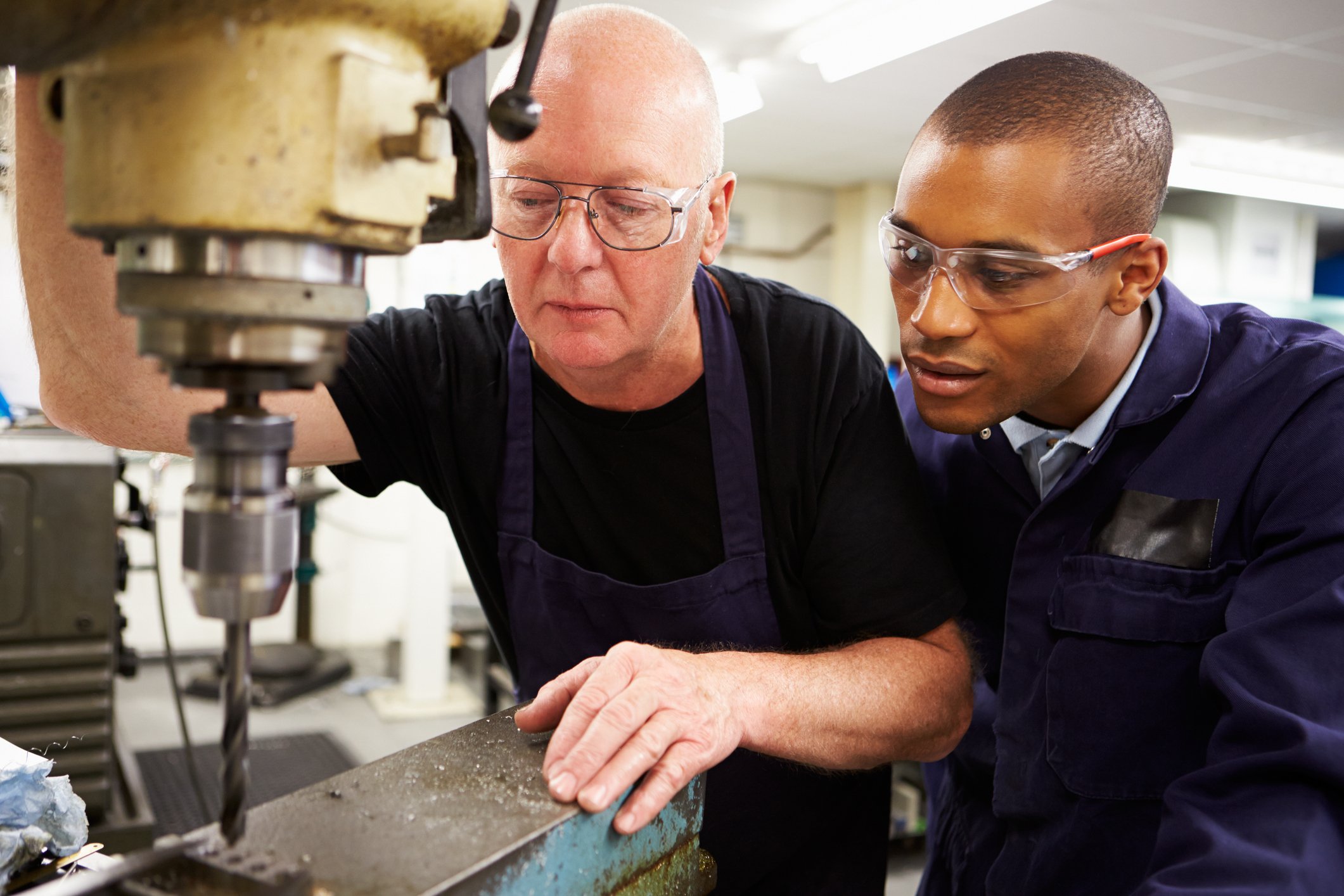 A man shows a younger man how to use a machine.