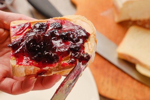 Peanut butter and jelly being spread on a slice of bread.