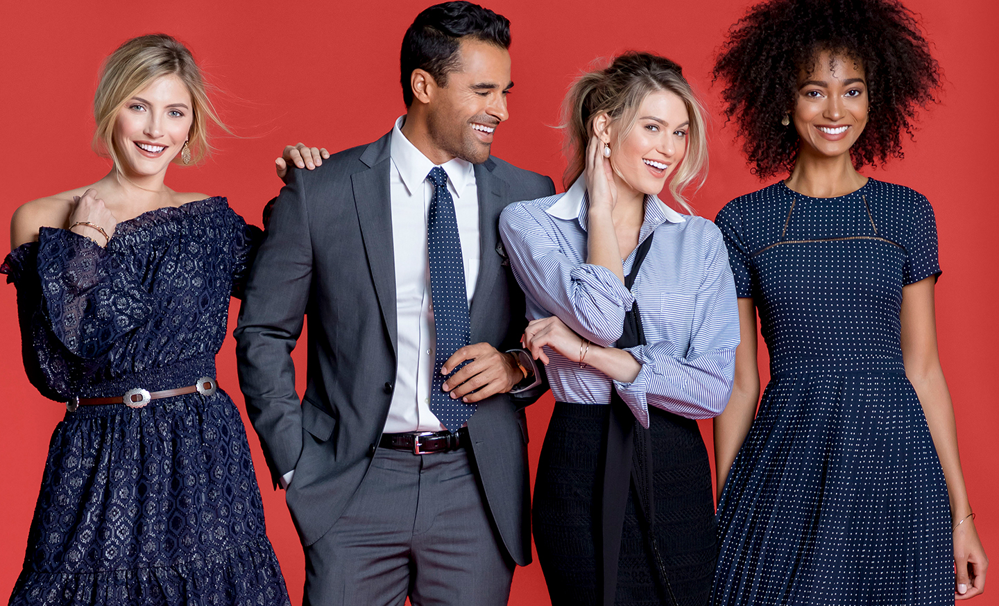 Three women and one man fashionably dressed smiling and posing.
