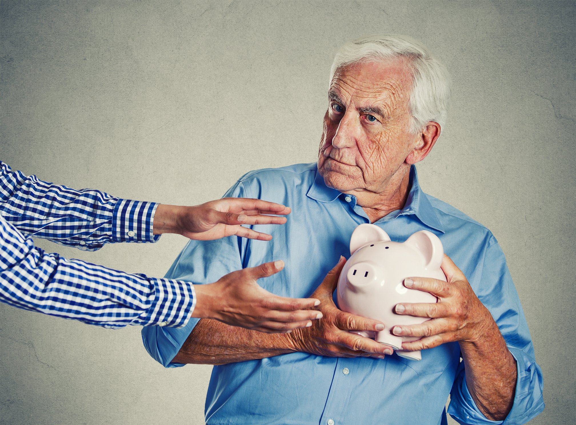 A senior man protects a piggy bank from someone trying to get it.