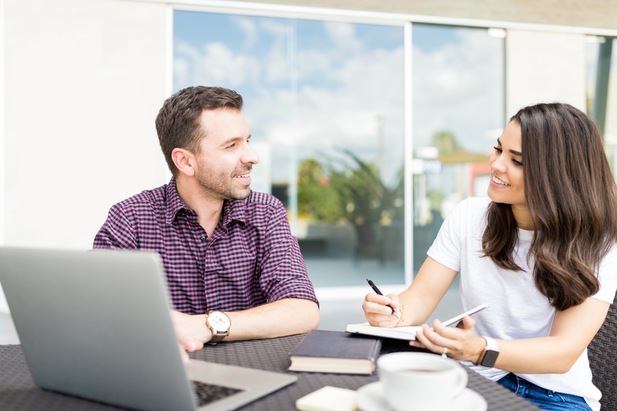 Two young Latin American people discuss business over a shared laptop.