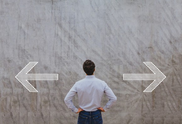 Man with hands on hips looking at arrows on a wall facing left and right