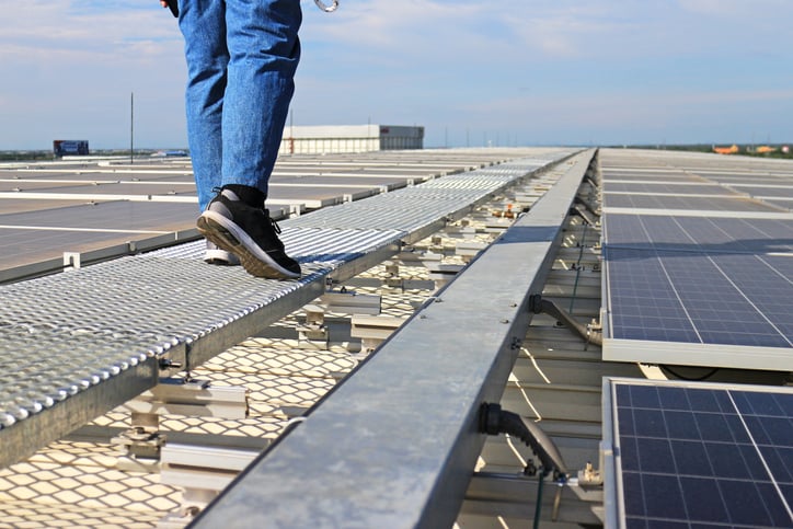 A man walking next to solar panels on a flat roof.