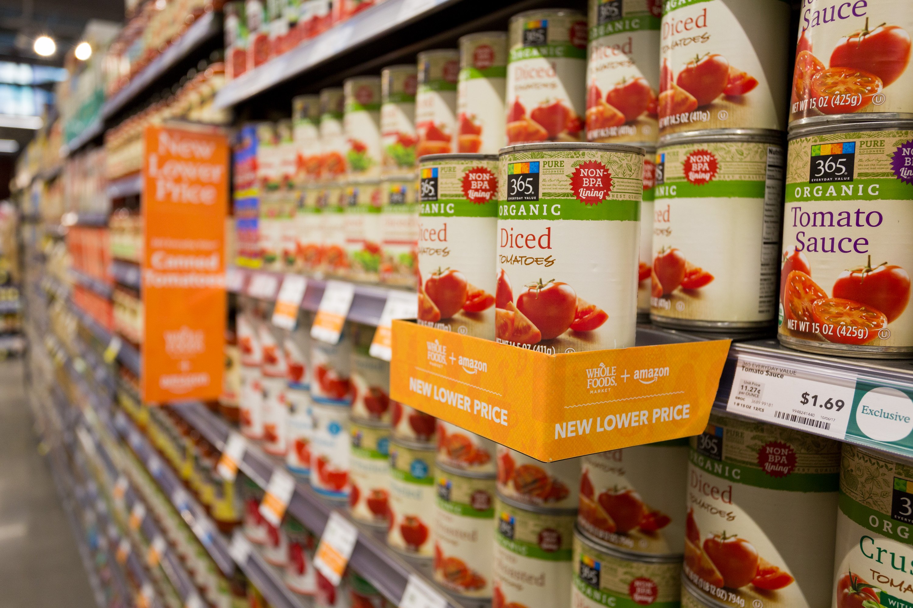 A shelf of canned tomatoes at Whole Foods with an Amazon notice about lower prices