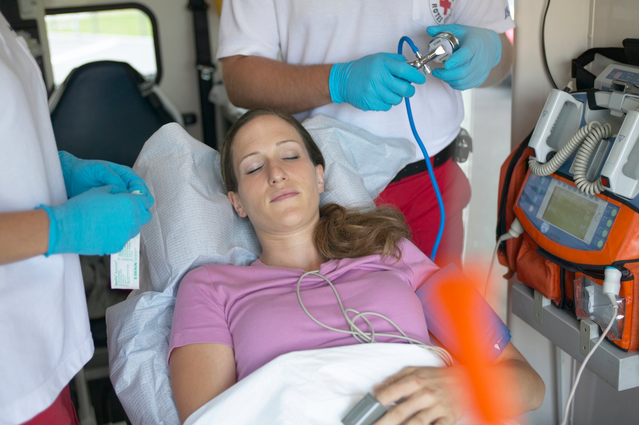 Woman lying down in an ambulance, being tended to by men wearing white shirts and blue gloves